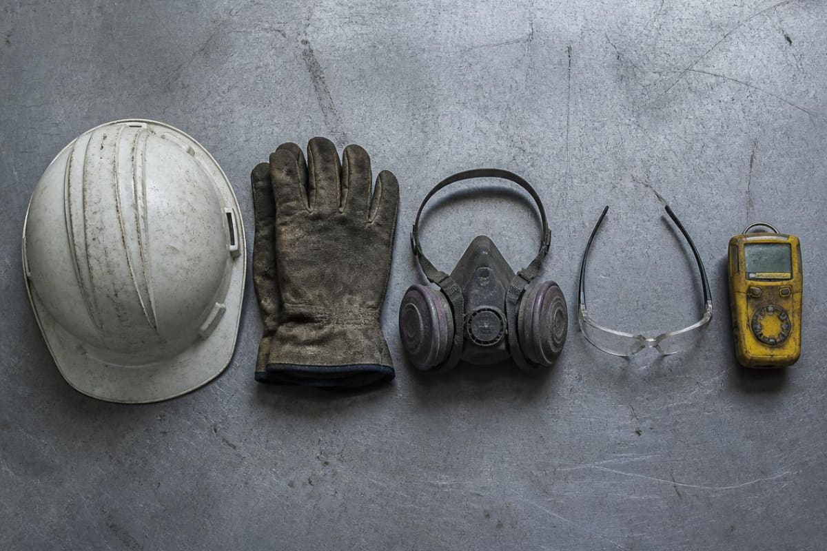 Helmet, gloves and respirator laid out on a steel bench