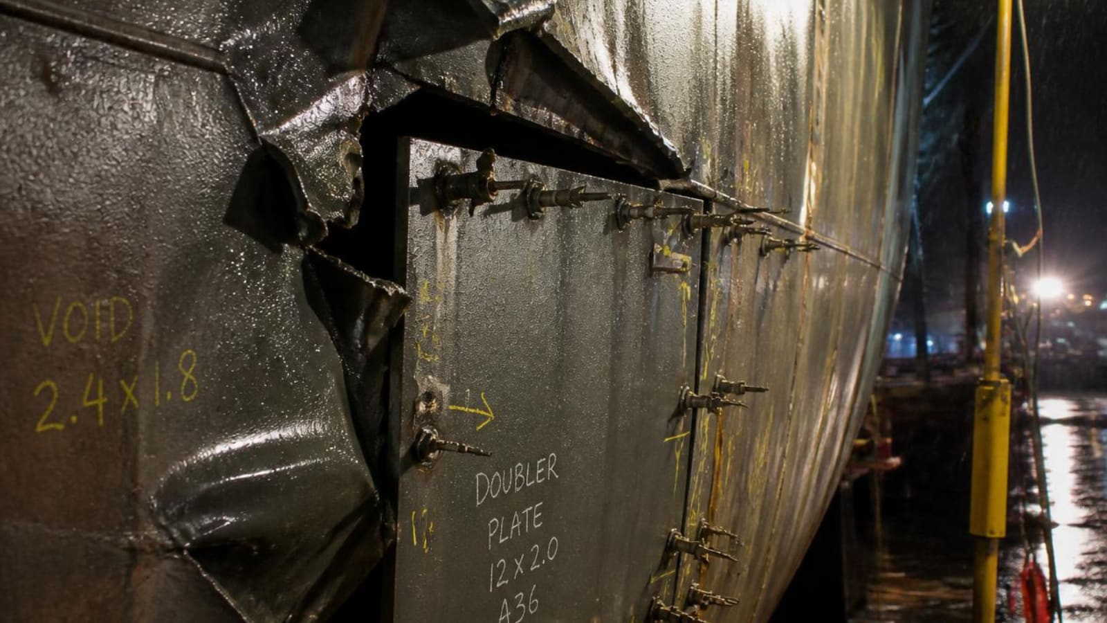 Damaged hull plating under repair at night beneath work lights